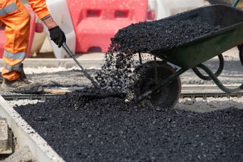 Construction worker pouring hot asphalt from a wheelbarrow onto a road surface outdoors